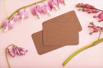 Brown business card with pink dicentra, broken heart flowers on pink pastel background. top view,