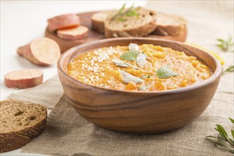 Sweet potato or batata cream soup with sesame seeds in a wooden bowl on a white wooden background