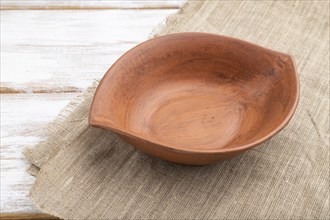 Empty clay brown bowl on white wooden background and linen textile. Side view, close up