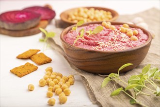 Hummus with beet and microgreen basil sprouts in wooden bowl on a white wooden background and linen