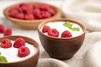 Yogurt with raspberry in clay cups on white wooden background and linen textile. Side view, close