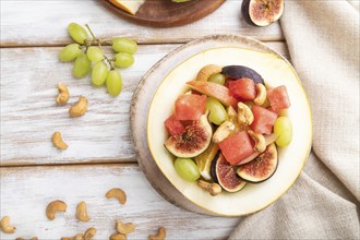 Vegetarian fruit salad of watermelon, grapes, figs, pear, orange, cashew on white wooden background