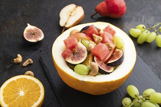 Vegetarian fruit salad of watermelon, grapes, figs, pear, orange, cashew on slate board on a black