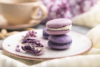 Purple macarons or macaroons cakes with cup of coffee on a gray wooden background and white linen