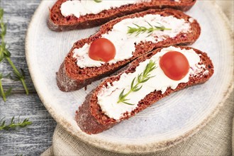 Red beet bread sandwiches with cream cheese and tomatoes on gray wooden background and linen