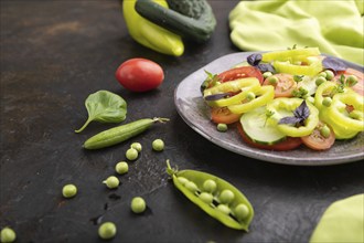 Vegetarian salad from green pea, tomatoes, pepper and basil on a black concrete background and