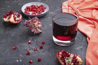 Glass of pomegranate juice on a black concrete background with red textile. Side view, close up