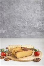 Smoked cheese and various types of cheese with rosemary and tomatoes on wooden board on a gray and