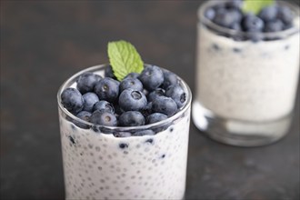 Yogurt with blueberry and chia in glass on black concrete background. Side view, close up