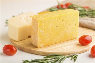 Various types of cheese with rosemary and tomatoes on wooden board on a white wooden background and