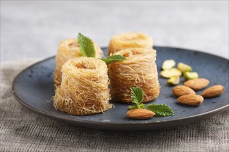 Kunafa, traditional arabic sweets in blue ceramic plate on a gray concrete background. side view,