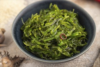 Chuka seaweed salad in blue ceramic bowl on brown concrete background. Side view, close up,