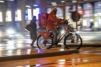 Street at the main station, Lieferando courier, cyclist, rainy weather, city centre, in the