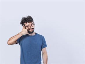 Attractive caucasian young male in casual clothes imitates telephone conversation, keeps hand near