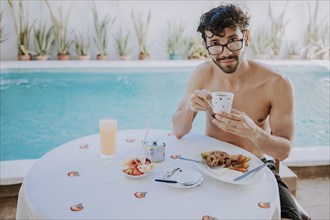 Breakfast near the swimming pool. Young man on vacation in hotel having breakfast near swimming