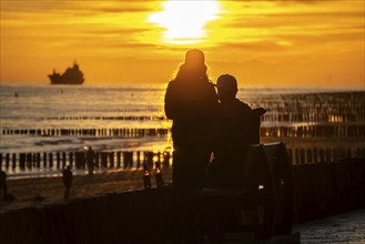 Sunset on the beach of Zoutelande, beach with wooden pile breakwaters, tourists, cargo ship sailing