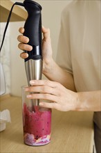 Closeup view of hands of a woman mixing fruits and berries in a blender for smoothie