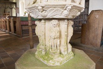 Stone carved lions and angels figures on baptismal font in village parish church of Saint John the