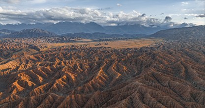 River bed runs through a landscape of eroded hills, badlands at sunset, mountain peaks of the Tian