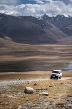 Off-road vehicle on a gravel track, glaciated and snow-covered peaks, Ak Shyrak Mountains, near