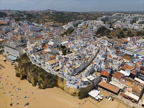 Coastal town with many white buildings on cliffs on the beach, sandy beach with bathers, aerial