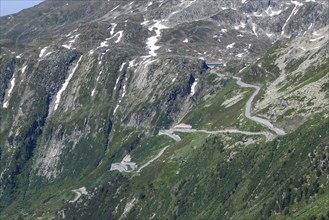 View of steep mountain road on slope above tree line with hairpin bends ascent to Grimsel Pass,