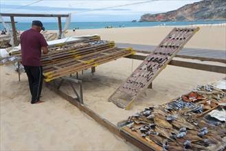 A man working on a wire rack with dried fish on the beach with sea view, fish drying, Praia da