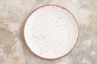 Empty white with dots ceramic plate on brown concrete background. Top view, copy space, flat lay