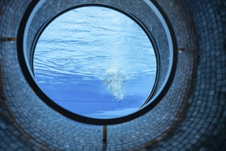 Woman Swimming in the Ship Porthole in Underwater in Swimming Pool in a Sunny Day in Switzerland