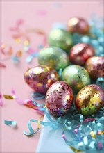 Small chocolate Easter eggs wrapped in shiny foil, placed on a bed of shredded pastel-colored