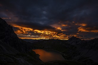 Lake Lüner See with Montafon mountains and dramatic cloudy sky at sunrise, Tschagguns, Rätikon,