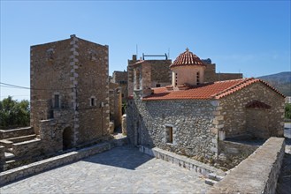 Traditional stone village buildings with red tiled roof under a blue sky, residential tower and