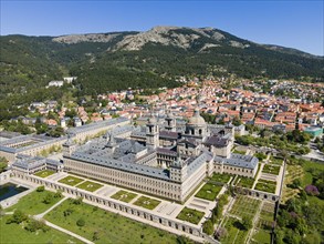 Historic monastery and neighbouring town, surrounded by green landscape and mountains, seen from