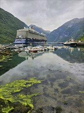 Large cruise ship, Mein Schiff 6 and boats sailing in a quiet fjord with green mountains and cloudy