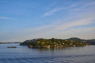 Small wooded island with houses in the sea with clear skies and calm water, Strusshamn, Bergen,