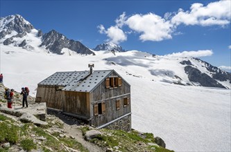 Mountaineer next to a mountain hut in front of a mountain landscape, Former hut of the mountain hut