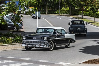 A black and white vintage car driving on a road in an urban environment, vintage car, Chevrolet Bel