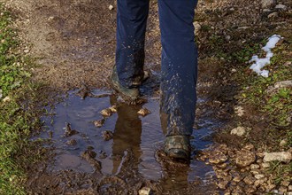 A person walks on a muddy path with puddles of water and wet sections