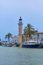 Harbour view with lighthouse, boats and palm trees in front of a clear blue sky, Le Grau-du-Roi,