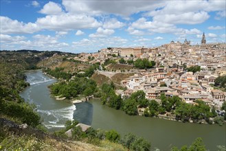 Panorama of a city on a hill with a river in the foreground and many houses under a blue sky with