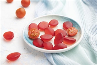 Jelly tomato candies on white concrete background and blue linen textile. close up, side view