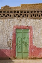 Green iron door in wall of traditional house made of mud and straw in the village Merzouga in the