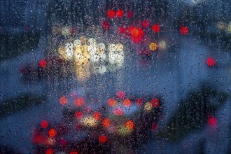 Rainy weather, road traffic, raindrops on a window pane, behind, blurred, lights of vehicles on a