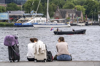 Tourists sitting at the back of Amsterdam Centraal railway station, on the banks of the river Ij,