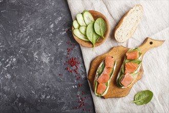 Smoked salmon sandwiches with cucumber and spinach on wooden board on a black concrete background.