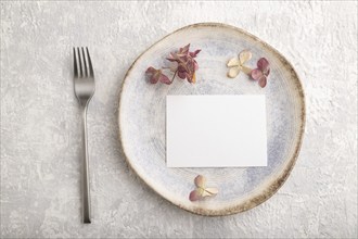 White paper invitation card, mockup with dried hydrangea flowers on ceramic plate and gray concrete