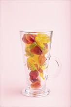 Various fruit jelly candies in drinking glass on pink pastel background. side view, close up