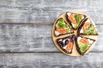 Grain rye bread sandwiches with cream cheese, tomatoes and microgreen on gray wooden background.