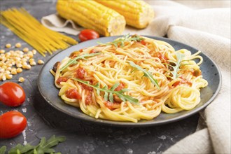 Corn noodles with tomato sauce and arugula on a black concrete background and linen textile. Side