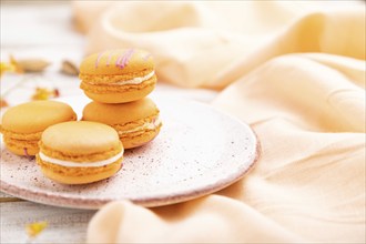 Orange macarons or macaroons cakes with cup of apricot juice on a white wooden background and